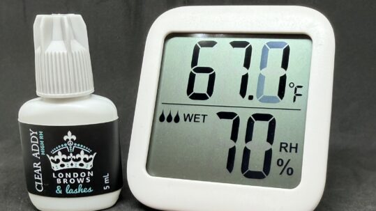 Clear lash adhesive beside hygrometer showing lash room humidity and temperature