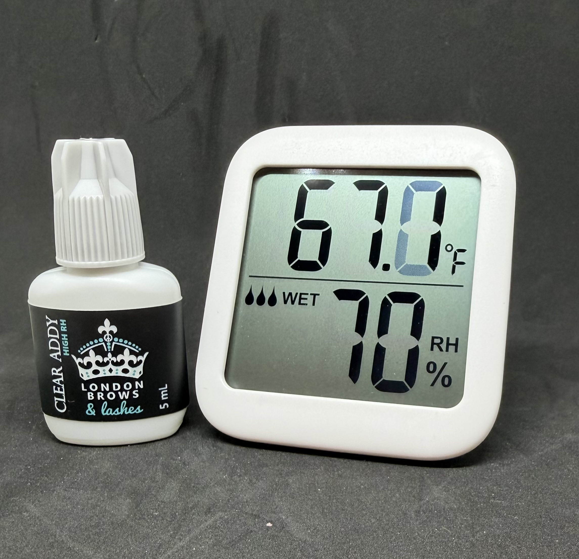 Clear lash adhesive beside hygrometer showing lash room humidity and temperature